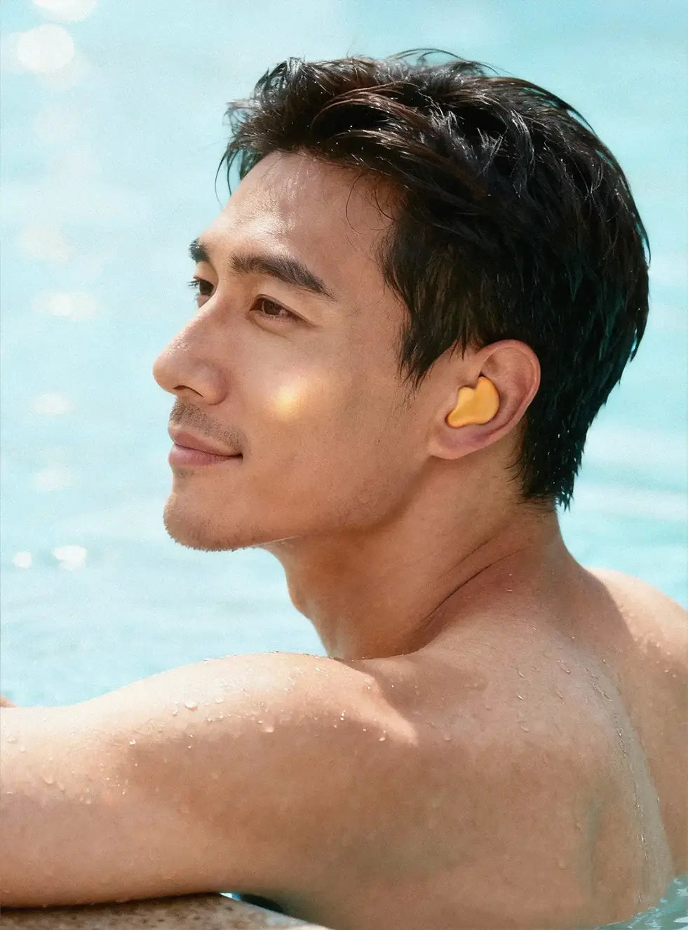 A man using waterproof yellow earplugs while resting by a swimming pool for total noise isolation and ear protection.